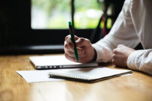 Man holding green pen while writing funeral service checklist